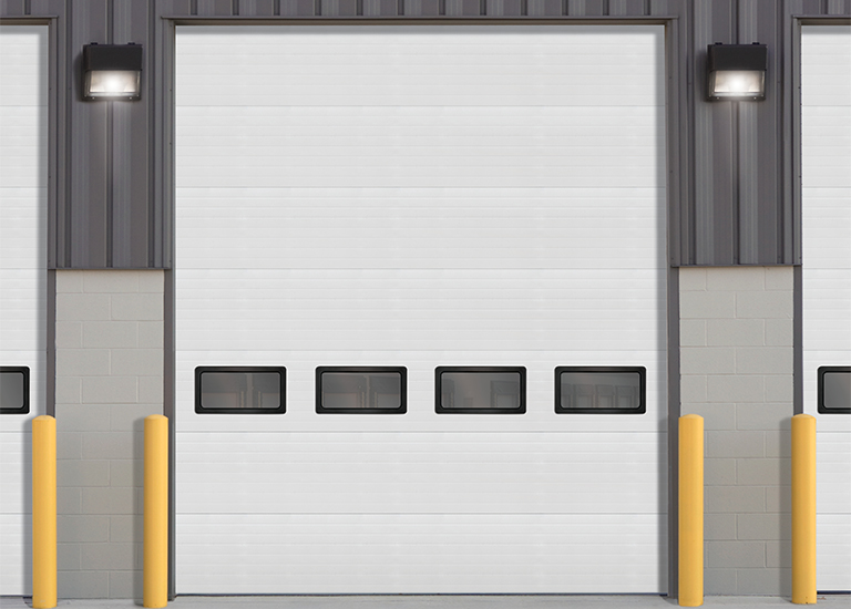 white commercial door on a buidling with four windows and four yellow bollards in front