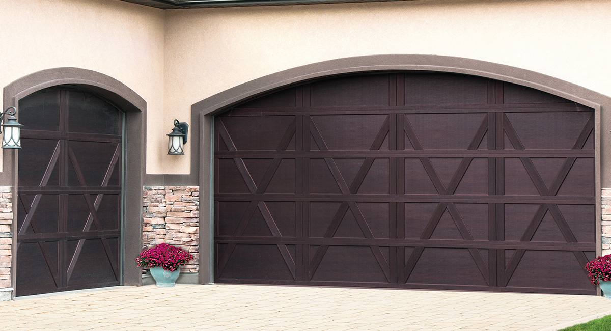 mahogany carriage house garage doors on tan home with red flowers and lights between the doors