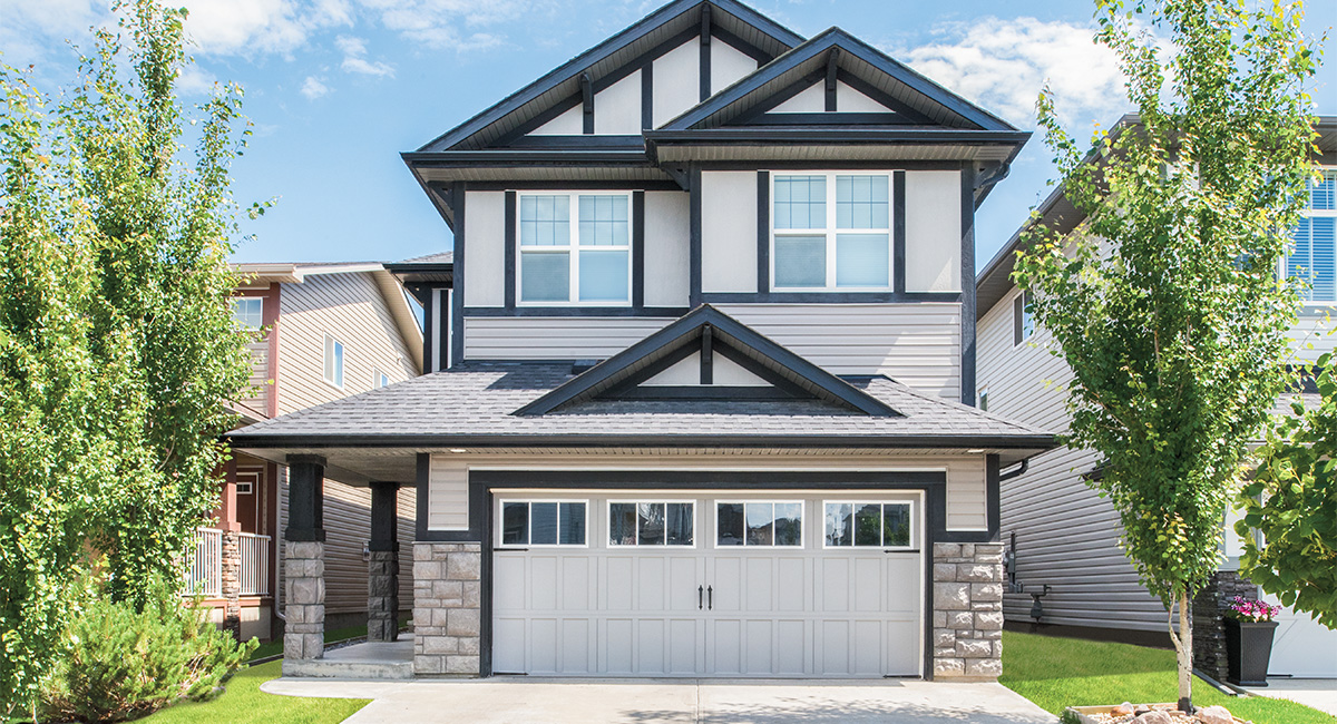 clay carriage house garage door on a house with two trees and blue sunny sky
